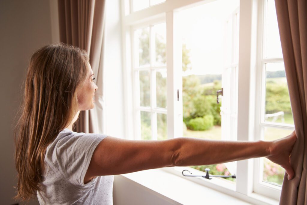 a woman opening window to let the fresh air in.