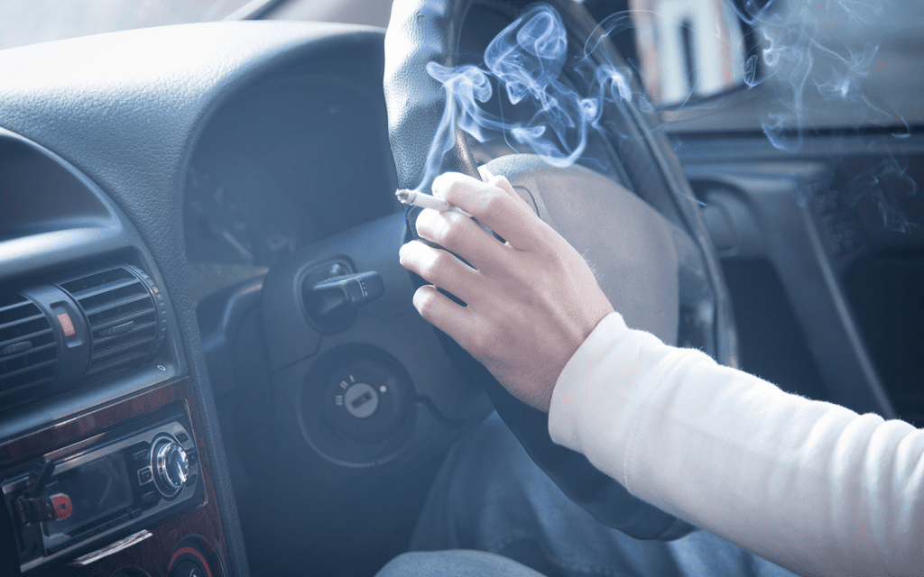 close shot of a hand on a car steering wheel with cigarette in hand.
